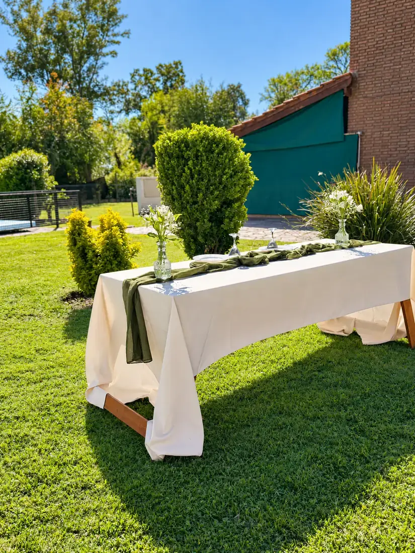 Mesa con mantel claro armada sobre el pasto junto a la casa